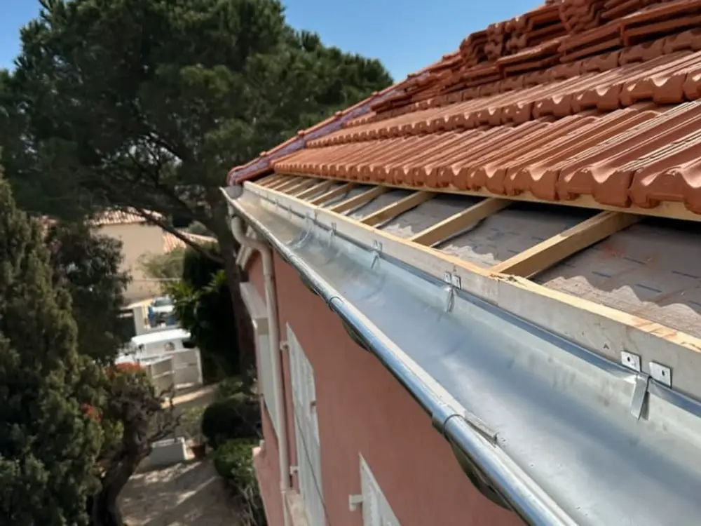 Gouttière en zinc neuve posée en bas de pente, liteaunage bois et écran sous-toiture visibles derrière