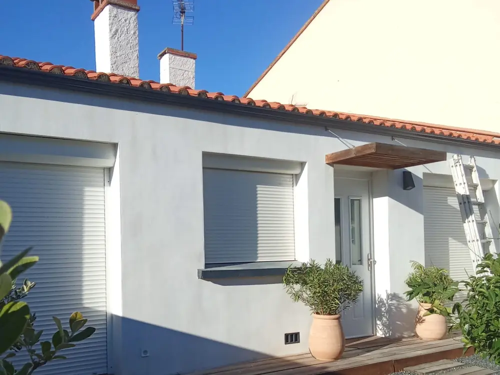 Façade à l’enduit clair avec volets roulants, sous une génoise et une rive de tuile canal